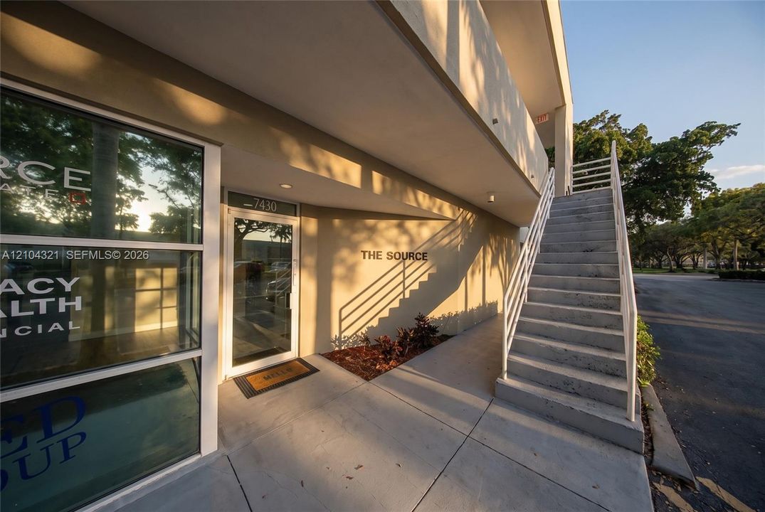 Exterior featuring a concrete staircase with metal railings, glass-paneled entry door, recessed lighting, and smooth-finish building facade