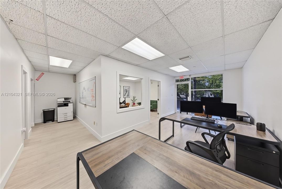 Workspace featuring wood-finish flooring, a suspended acoustic tile ceiling with recessed lighting, an interior glass partition, and a large window