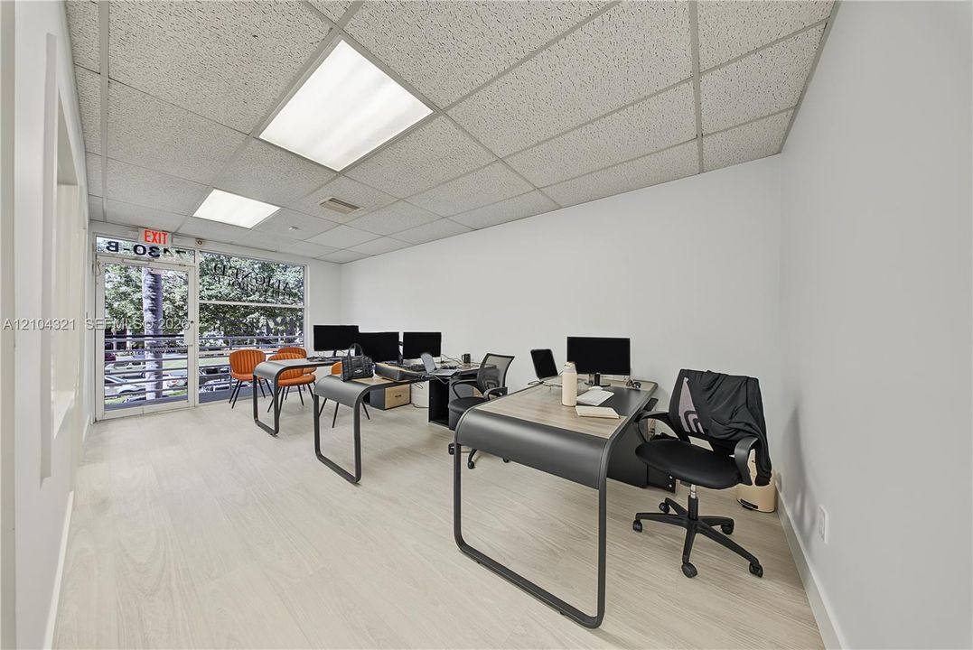 Open-concept interior featuring light wood-finish flooring, drop ceiling with integrated recessed lighting, and a glass-paneled exterior door
