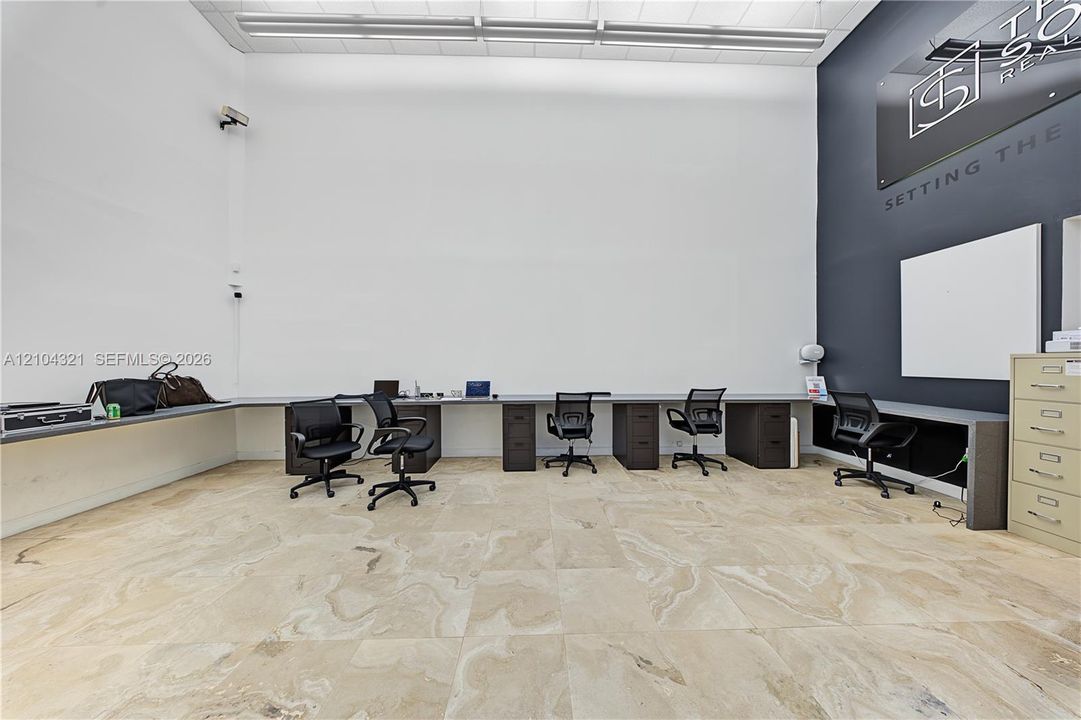 High-ceilinged room featuring neutral large-format tile flooring, integrated perimeter desk cabinetry, and a charcoal accent wall