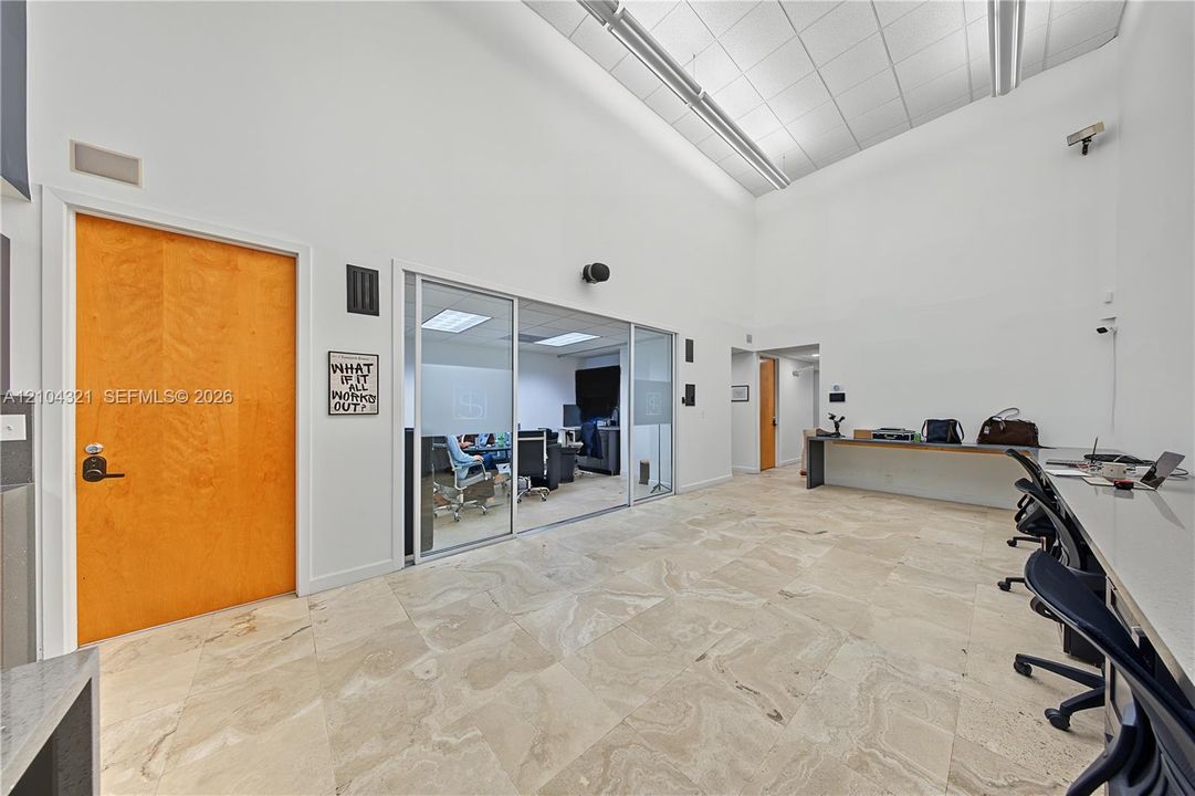 High-ceiling interior space featuring large-format stone flooring, a glass-panel sliding door, a built-in stone-surface desk, and a solid wood-veneer door