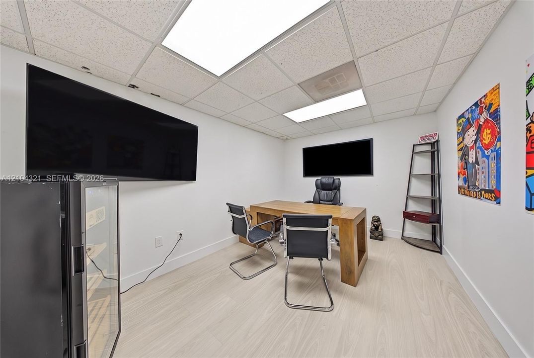 Interior room featuring light-toned wood-finish flooring, white walls, and a drop ceiling with integrated rectangular lighting panels