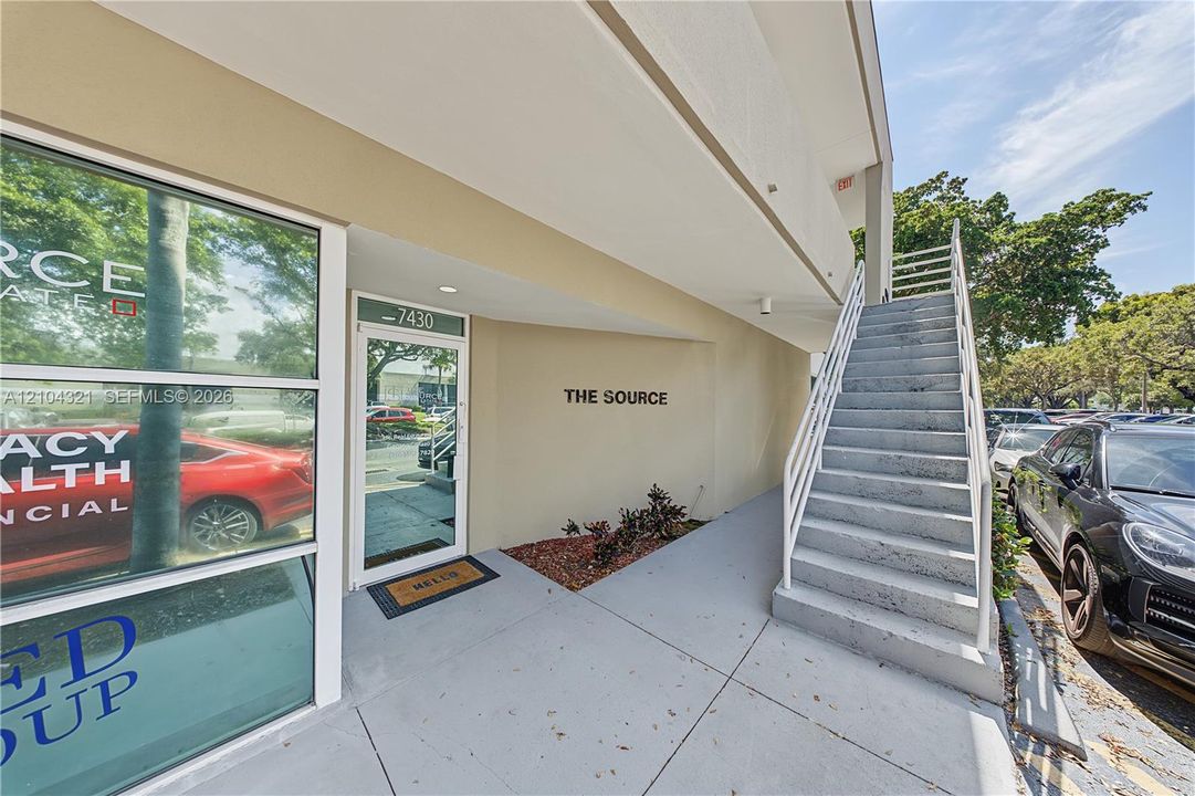 Exterior entry featuring a glass-paneled storefront door, concrete walkway, and metal staircase with handrails