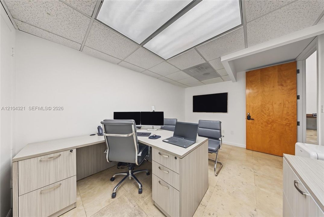 Room featuring drop ceiling tiles, recessed rectangular fluorescent lighting, natural stone-finish flooring, and a solid wood-finish door