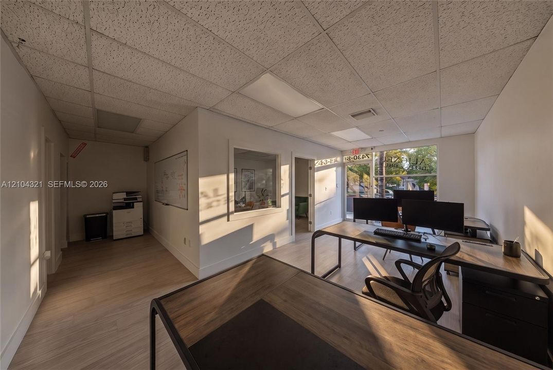 Interior space featuring wood-finish flooring, a suspended grid ceiling, neutral wall finishes, a built-in interior window, and large glass storefront entry