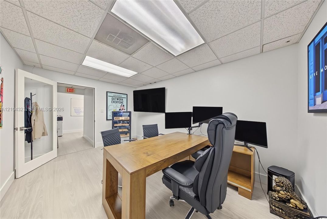 Room featuring wood-finish flooring, recessed drop ceiling with integrated lighting, and a white-framed glass pane door