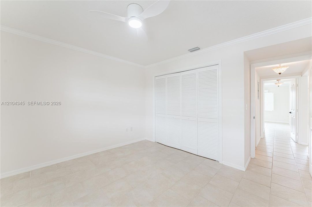 Neutral-toned tile flooring, white louvered closet doors, and modern ceiling fan with integrated lighting