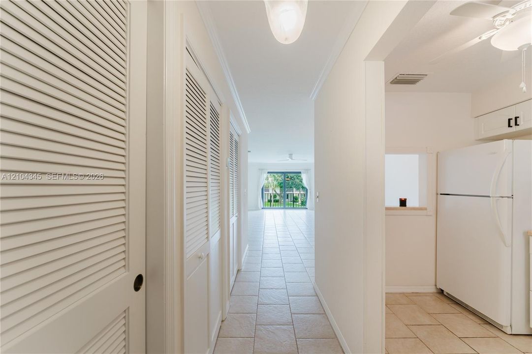 Neutral-toned tile flooring, white louvered closet doors, and a built-in kitchen pass-through window