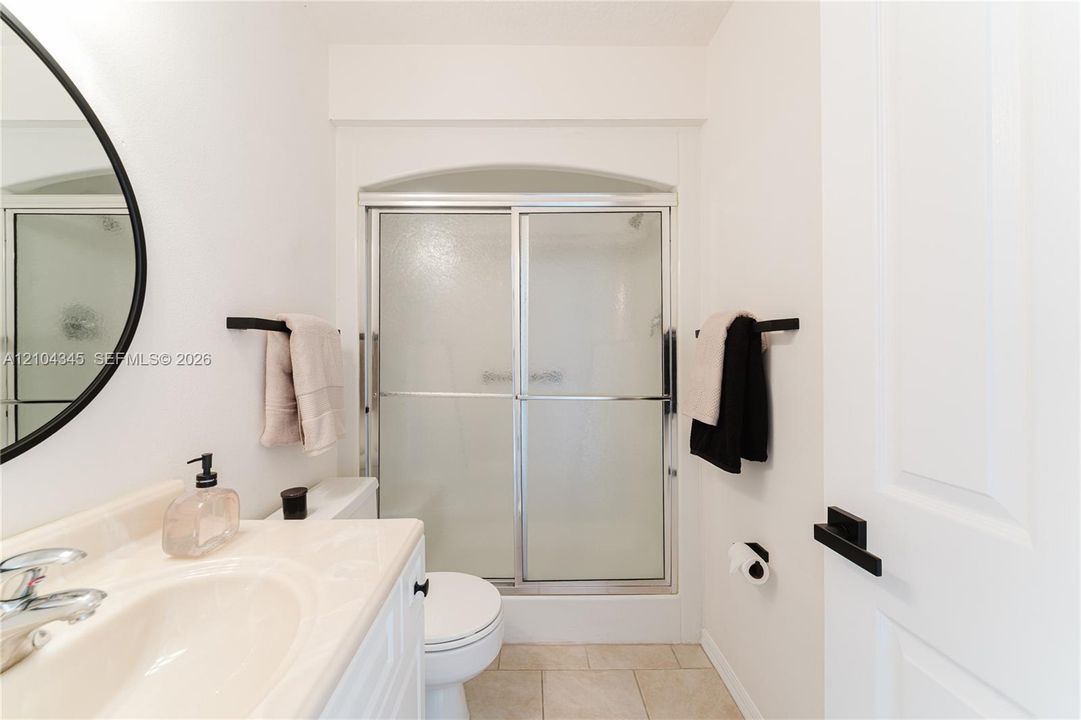 Ensuite bathroom featuring a vanity with an integrated sink, matte black hardware, a round mirror, and a shower with sliding glass doors