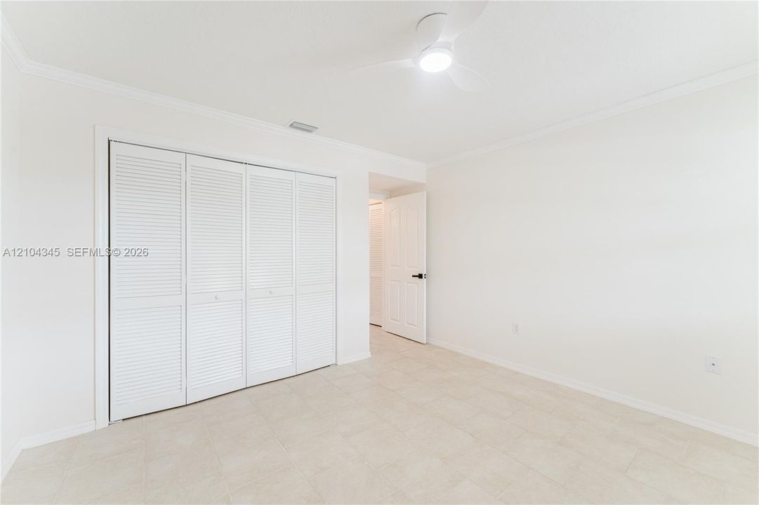 Neutral interior featuring light tile flooring, white walls with crown molding, four-panel louvered closet doors, and a ceiling-mounted LED fan