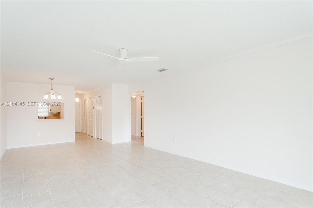 Open-concept interior featuring neutral tile flooring, a minimalist white ceiling fan, multi-light chandeliers, and a wall cutout pass-through