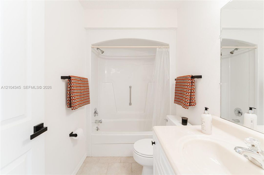 Full Second bathroom featuring a tub-shower combination with an arched alcove, vanity with an integrated sink, polished chrome plumbing fixtures, and matte black hardware