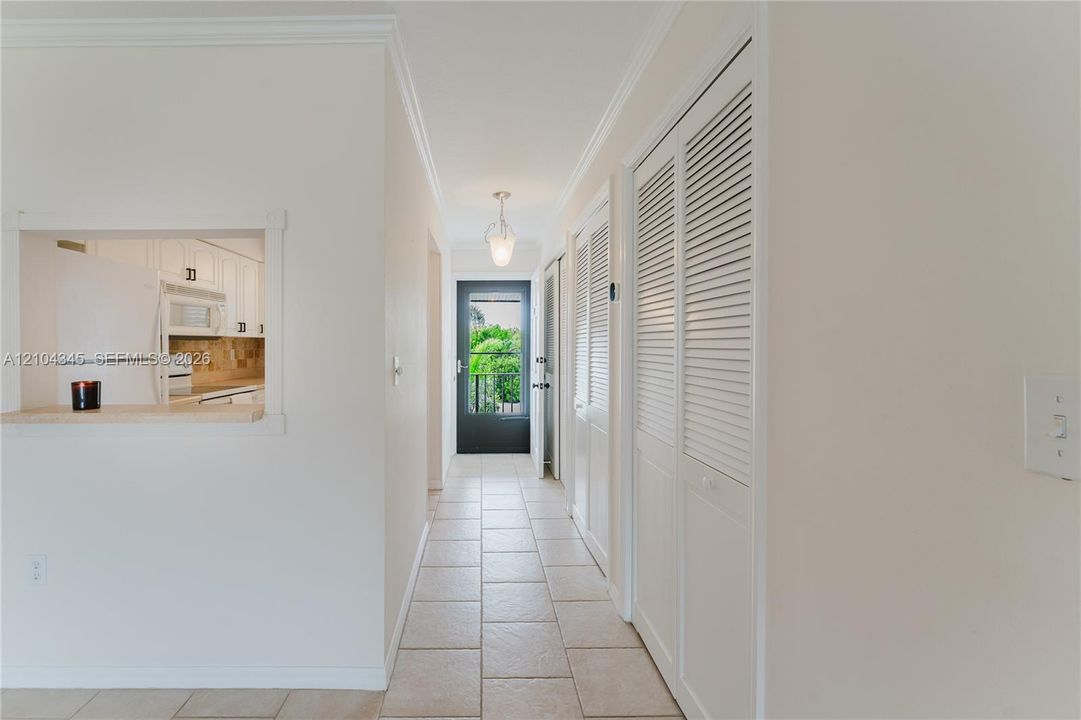 Hallway featuring tile flooring, louvered bi-fold closet doors, a pendant light fixture, and a pass-through opening