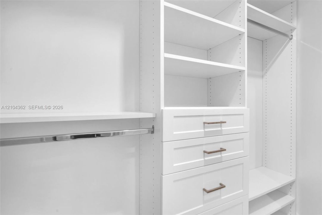 Custom white cabinetry featuring adjustable shelving, integrated drawer units, metal garment rods, and hardware with a metallic finish