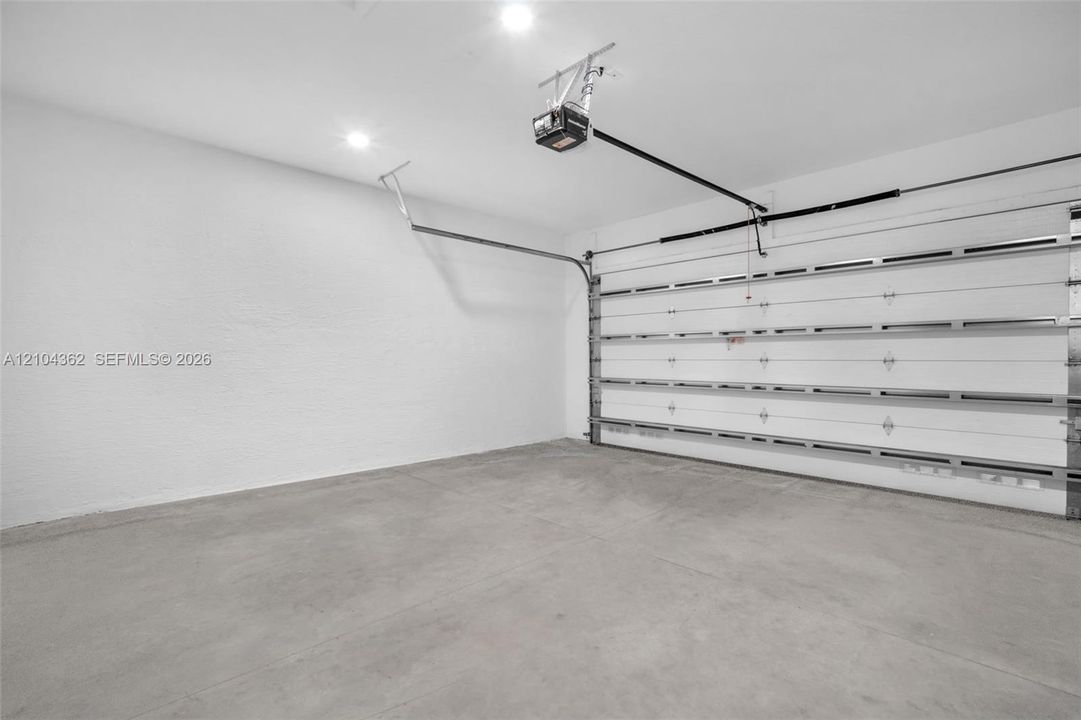 Garage interior featuring a concrete floor, finished white walls, recessed ceiling lighting, and a motorized garage door opener