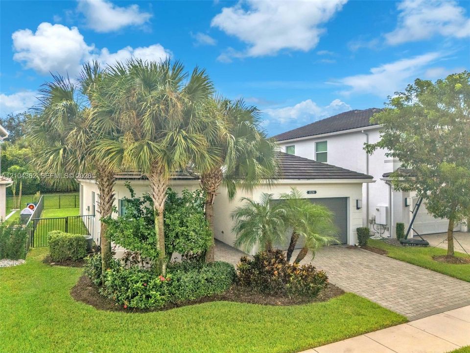 Stucco exterior featuring a multi-hipped tile roof, paved driveway, two-car garage, and established landscaping with mature palm trees