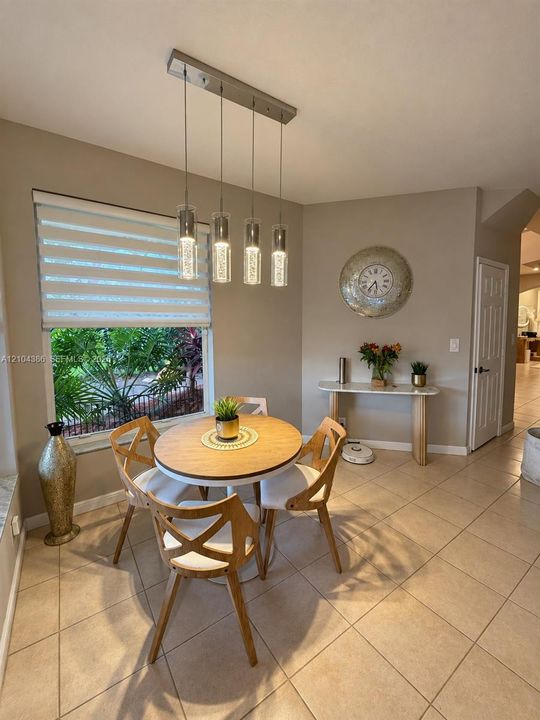 Dining area featuring neutral tile flooring, multi-light pendant fixture, and large windows equipped with dual-layered roller shades