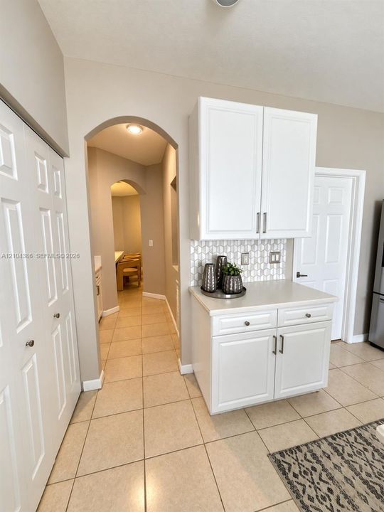 Kitchen featuring white shaker-style cabinetry, central island with a solid-surface countertop, mosaic tile backsplash, stainless steel refrigerator, and ceramic tile flooring