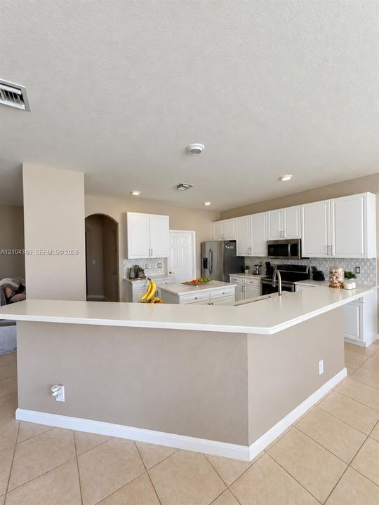 Neutral-toned walls paired with large-format tile flooring, featuring a linear four-pendant light fixture and a multi-pane window with integrated roller shades