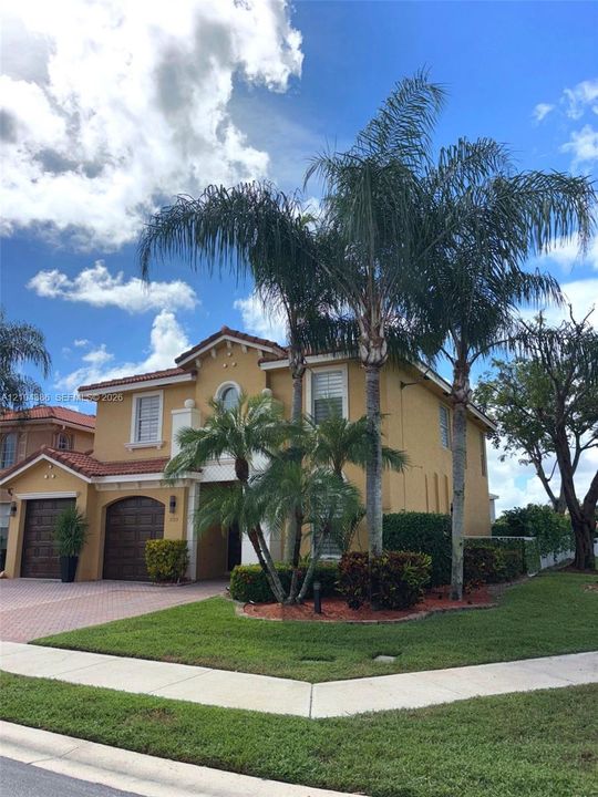 Two-story exterior featuring a stucco façade, herringbone-patterned paver driveway, arched garage doors, and a tile roof