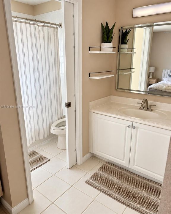 Bathroom featuring white cabinetry, an integrated sink with a metallic faucet, a vanity mirror with integrated LED lighting, and a walk-in shower with a glass sliding enclosure and tile flooring