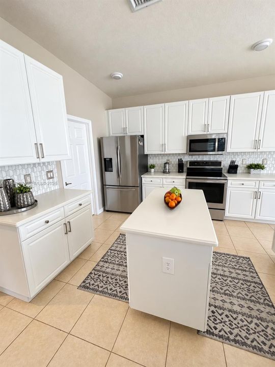 Kitchen pass-through featuring white cabinetry, solid surface countertop, built-in sink, and ceramic tile flooring