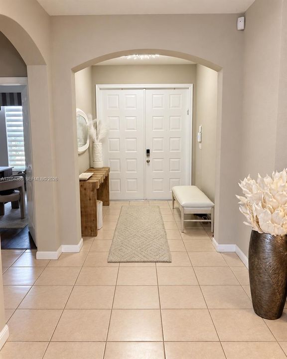Two-story foyer featuring high ceilings, neutral wall tones, ceramic tile flooring, and a staircase with white balusters and handrails