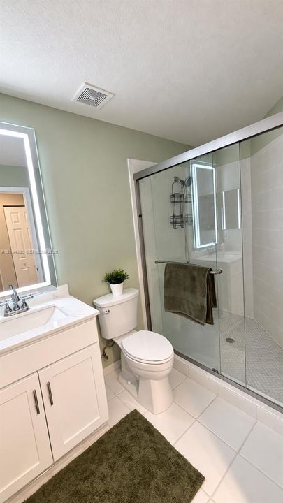 Bathroom featuring a vanity with a white countertop and oval under-mount sink, full-width wall mirror, arched light fixture, ceramic tile flooring, and multi-panel doors