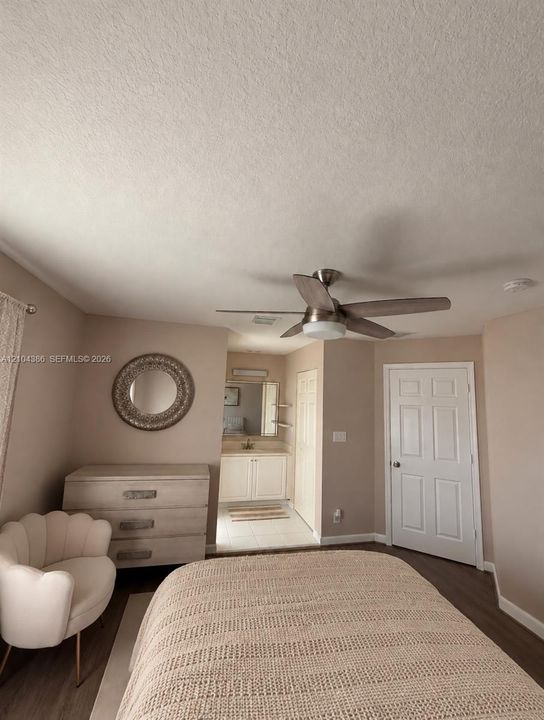 Bedroom interior featuring wood-finish flooring, a neutral-toned wall finish, a multi-blade ceiling fan with an integrated light fixture, and a white paneled closet door