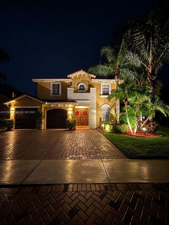 Stucco exterior featuring decorative corbels, clay-tile roofing, arched multi-lite windows, a paver driveway, and a double-entry door system