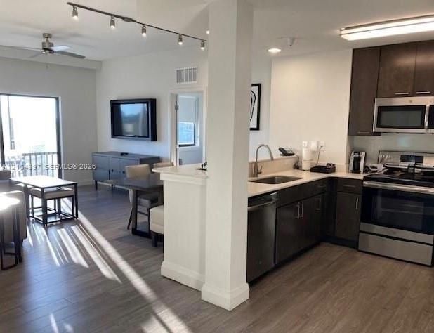 Open-concept living space featuring wood-finish flooring, dark cabinetry, stainless steel appliances, quartz countertops, and track lighting