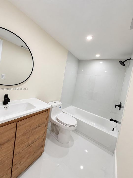 Bathroom featuring a wood-finish vanity with a white countertop, circular wall-mounted mirror, matte black plumbing fixtures, and a tub-shower combination with floor-to-ceiling tile surround