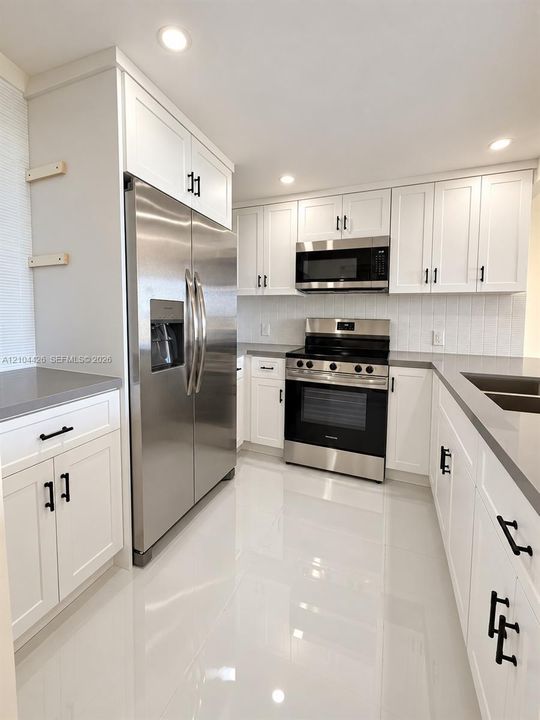 Kitchen featuring white shaker-style cabinetry, quartz countertops, stainless steel appliances, vertical tile backsplash, and polished tile flooring