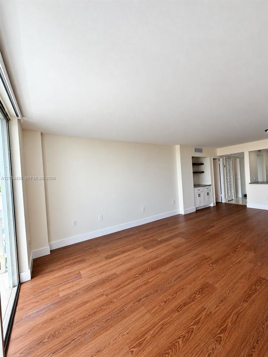 Wood-finish flooring, floor-to-ceiling glass sliding doors, and built-in cabinetry featuring lower storage and open shelving