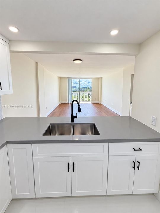 Kitchen featuring white shaker-style cabinetry, matte black hardware, quartz countertops, a dual-basin stainless steel sink with a high-arch faucet, and wood-finish flooring