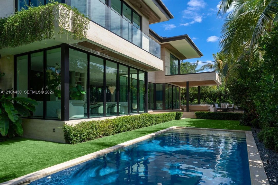 Modern exterior featuring floor-to-ceiling glass walls, stacked stone facade, expansive second-level glass balcony railings, and a rectangular swimming pool set within a manicured landscape