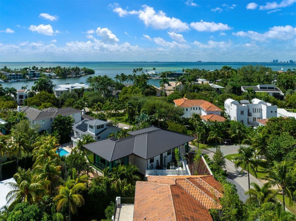 Aerial perspective featuring a metal roof structure, terracotta tile roofing, mature landscaping, and proximity to the coastline