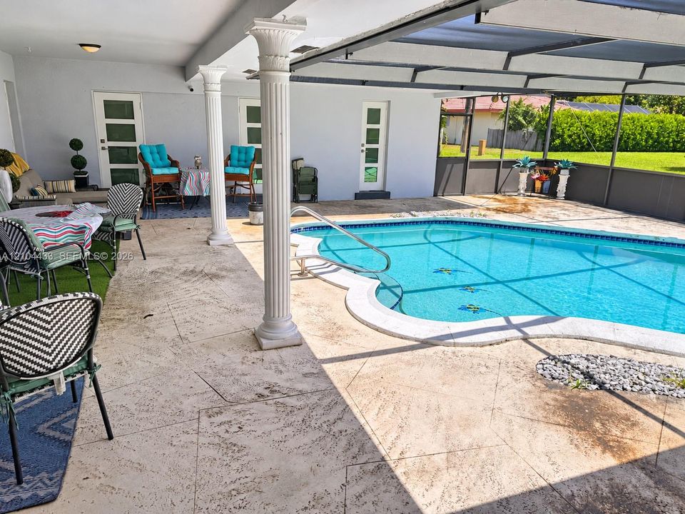Expansive outdoor patio with a freeform swimming pool, decorative columns, and a screened enclosure