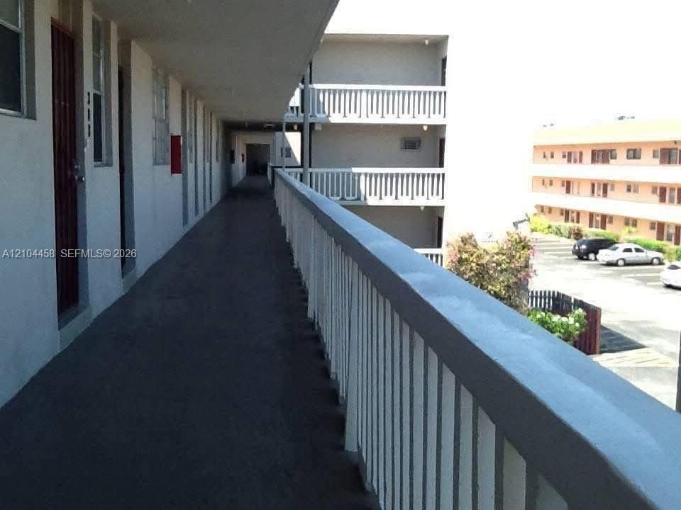 Exterior covered walkway featuring white metal railings and painted concrete surfacing