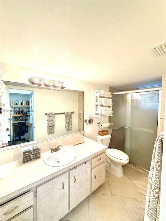 Vanity with integrated sink and stone-surface countertop, full-width wall mirror, four-light vanity fixture, walk-in shower with glass enclosure, and tile flooring
