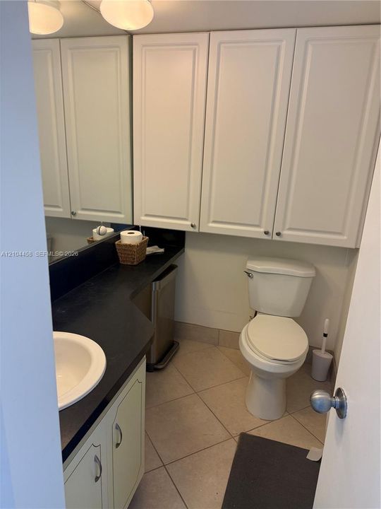 Vanity featuring a dark countertop, white cabinetry, a recessed sink, wall-mounted upper storage cabinets, and tile flooring