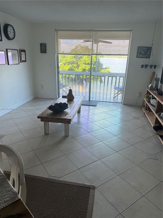 Large-format ceramic tile flooring, sliding glass door with roller shade, and attached balcony featuring a water backdrop