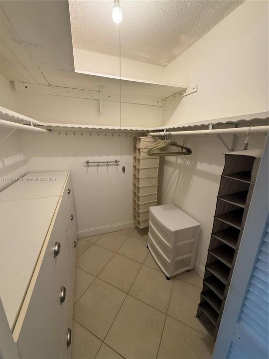Walk-in closet featuring white built-in cabinetry, ceramic tile flooring, and integrated white shelving