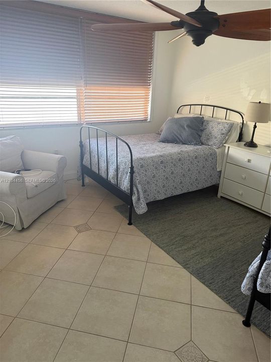 Large-format tile flooring, multi-pane window with horizontal blinds, and a ceiling-mounted fan with wood-finish blades