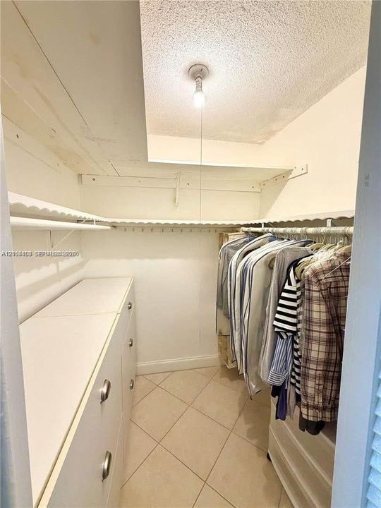 Storage space featuring built-in cabinetry, upper shelving with integrated hanging rods, and tile flooring