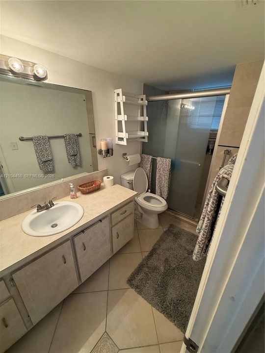 Bathroom featuring a vanity with a drop-in sink, stone-finish countertop, large wall-mounted mirror, ceramic tile flooring, and a walk-in shower enclosure with a sliding glass door