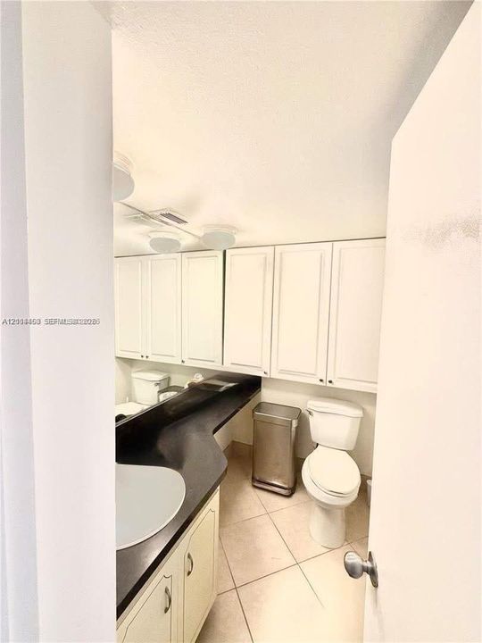 Bathroom featuring white shaker-style cabinetry, dark countertop, integrated sink, and ceramic tile flooring