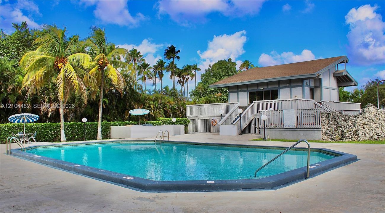In-ground swimming pool with a concrete deck, built-in stone-accented wall, and exterior structure featuring a second-level deck with wooden staircase