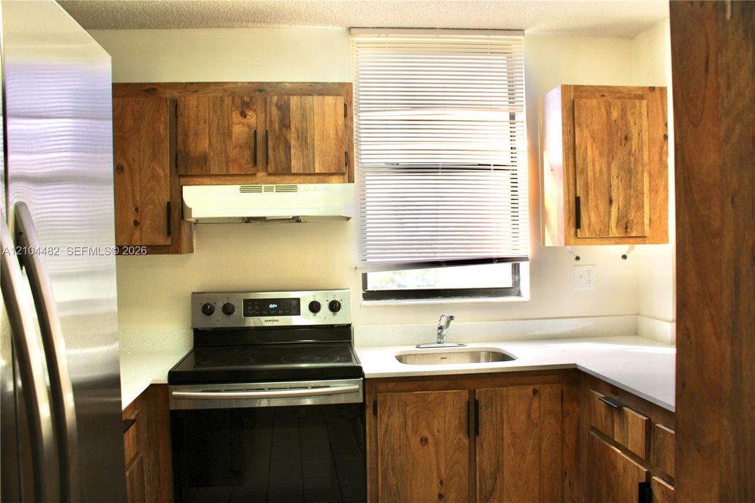 stainless steel appliances, solid surface countertops, a stainless steel sink, and a window with horizontal blinds