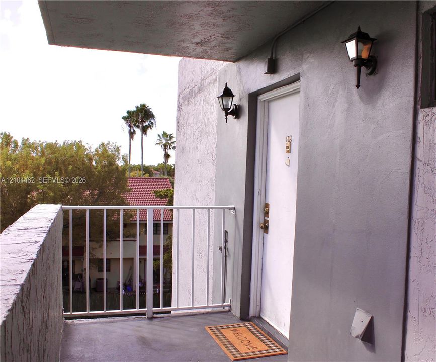 Covered balcony entryway featuring a painted concrete surface, white metal railings, and dual wall-mounted exterior lanterns